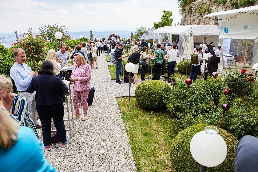 Mitarbeiter:innen in einem Garten mit Stehtischen und Zelten- mit Ausblick über Linz.