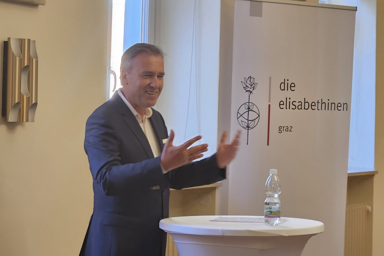Christian Jauk beim Halten eines Vortrages, hinter einem Stehtisch. Im Hintergrund ein Roll-up mit dem Elisabethinen Logo.