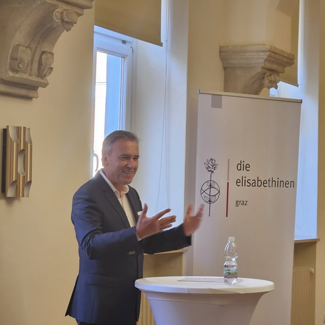 Christian Jauk beim Halten eines Vortrags, vor einem Rollup mit Elisabethinen Logo.